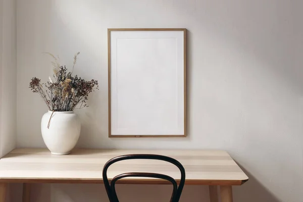 Oturma odası, sakin bir hayat. Ahşap masa, masa ve eski sandalye üzerindeki boş çerçeve modeli. Kuru otlu beyaz vazo. Zarif çalışma alanı, ev ofisi konsepti. İskandinav iç tasarımı. — Stok fotoğraf