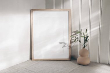 Portre boş ahşap çerçeve, güneş ışığında modelleme. Modern organik vazoda zeytin dalı. Bej keten masa örtüsü. Beyaz wainscot duvar kaplama arka planı. İskandinav iç mimarisi, ev tasarımı. Sanat