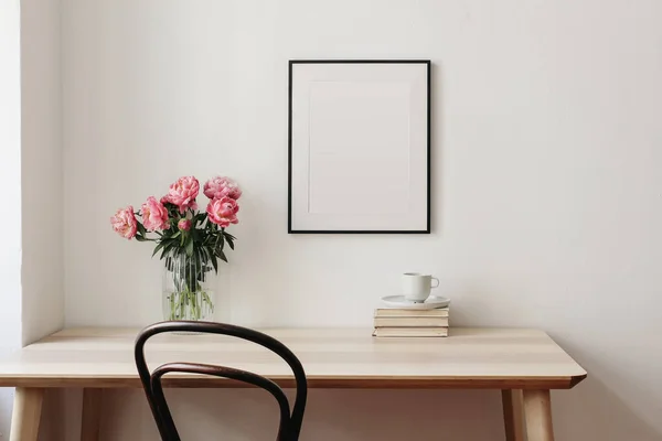 Salon, nature morte intérieure. Cadre photo vide maquette sur mur beige. Table en bois et vieille chaise. Vase en verre avec bouquet de pivoines roses. Espace de travail élégant, concept de bureau à domicile. Design d'intérieur. — Photo