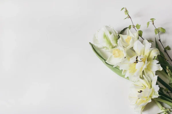 Ženská květinová kompozice. Dekorativní webový prapor z krásných bílých a žlutých tulipánů. Daffodils květiny s březovými větvemi. Bílé pozadí. Prázdné místo. Stylová rovina, pohled shora. — Stock fotografie