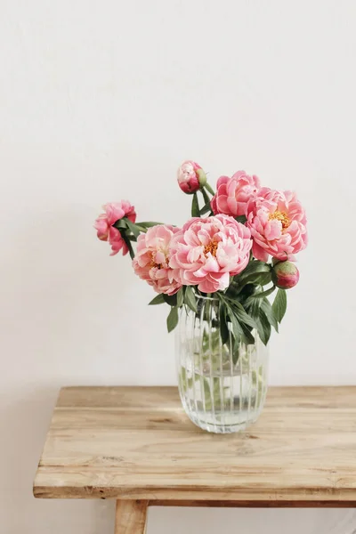 Floral ainda cena da vida. Flores de peônias cor-de-rosa, buquê em vaso de vidro na mesa de madeira. Parede branca. Foco seletivo, fundo turvo. Casamento, conceito de comemoração de aniversário. Estilo de vida foto vertical — Fotografia de Stock