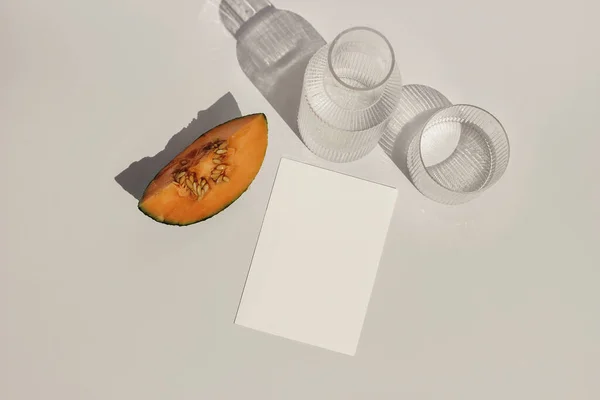 Summer food still life composition. Cantaloupe melon fruit. Beige table background. Stationery mock up scene. Blank paper card, invitation. Carafe and glass of water, cocktail in sunlight. Flat lay — Foto de Stock