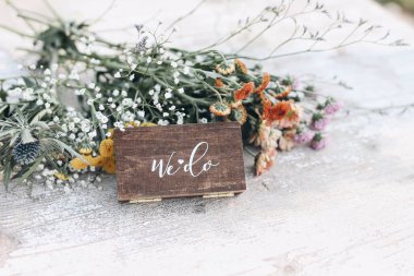 Boho düğünü hala hayattadır. Beyaz harfli yüzükler için takı ahşap bir hediye. Beyaz mahsul arka planında annelerin çiçekleri olan renkli bir çiçek buketi. Evlilik, nişan konsepti. Seçici odak