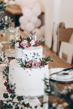 Şık bir düğün sofrası. Süslü, çıplak pasta, beyaz krema, çiçekler ve meyve. Lüks yemekler, hamur işleri. Seçici odaklanma, dikey. Doğum günü partisi zamanı. Çilekli süsleme.