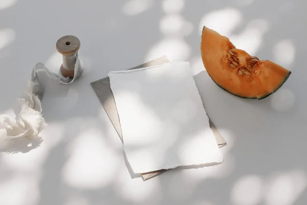 Summer food still life composition. Cantaloupe melon fruit, silk ribbon. White table background with tree shadows overlay. Stationery mock up scene. Blank paper card, invitation in sunlight. Top view — Foto de Stock