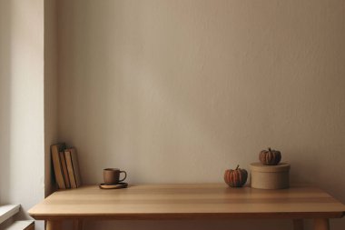 Autumn interior still life. Scandinavian living room, home office. Pumpkins, books, gift box, coffee cup on table. Fall, Halloween or Thanksgiving holiday home decor, empty beige wall mockup background.
