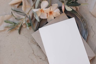 Boş Beyaz Düğün Davetiye Kartı Bej Zarflı, Yumuşak Şeftali Oleander Çiçekleri ve Mermer Arkaplanda Zeytin dallı. Zarif Yaz Düğün Yassı Kırtasiye Sahnesi. Boş Kopyalama Boşluğu