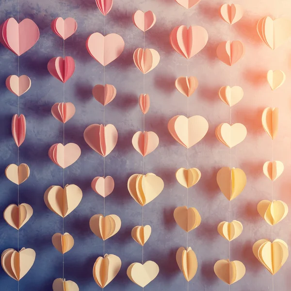 Bunte Herzen Papiergirlanden hängen an der Wand. Der Hintergrund des romantischen Valentinstages. Foto im Instagram-Stil getönt. — Stockfoto