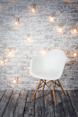 Empty white chair against the backdrop of a brick wall with a garland of light bulbs.