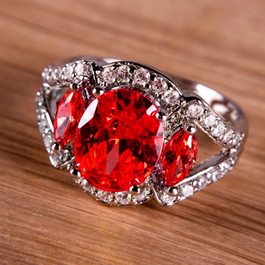 Macro view of silver or white gold ring with red gems and diamonds on wooden background.
