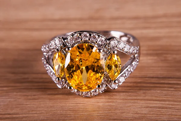 Macro view of silver or white gold ring with yellow gems and diamonds on wooden background. — 图库照片