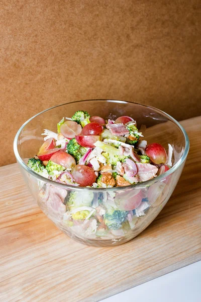 Fresh salad with bacon, grapes, walnuts, greens and herbs and olive oil in transparent glass salad-bowl. Portion of salad on the background of cardboard with space for your text. — Stockfoto