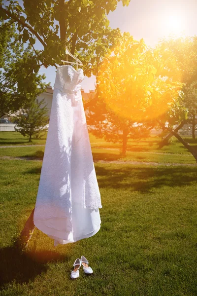 Wedding dress hanging on a tree in the park and white ladies shoes — Stock Photo, Image