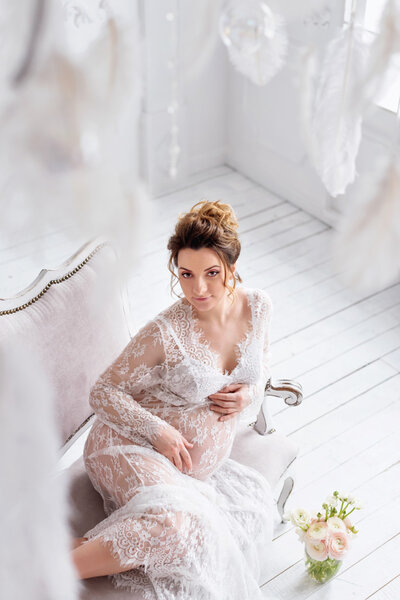 Young pregnant woman wearing lace dress in white interior. Fashion shot.