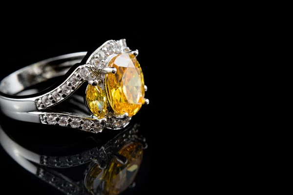 Inel de aur argintiu sau alb cu pietre galbene și diamante pe fundal de sticlă neagră . — Fotografie, imagine de stoc