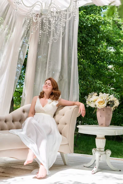 Mujer bonita divirtiéndose en el gazebo jardín de verano. Opulenta sala de estar al aire libre con flores para la celebración, fiesta de té . — Foto de Stock