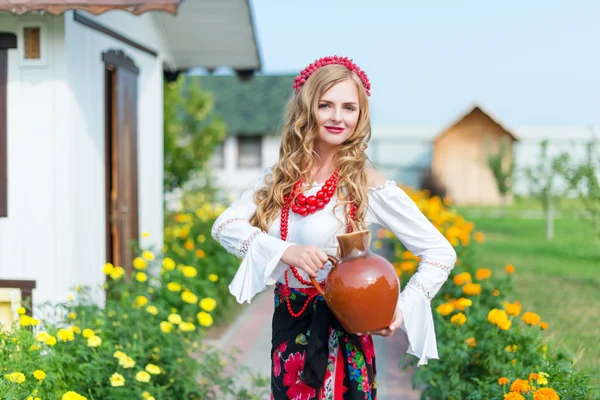 Woman in national ukrainian traditional costume holding a clay jug and welcoming guests — Stock Photo, Image