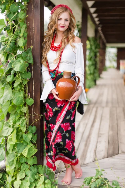 Vrouw in Oekraïense traditionele klederdracht holding een kruik van klei en het verwelkomen van gasten — Stockfoto