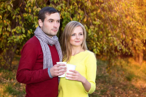Love, relationship, season, friendship and people concept - happy man and woman enjoying golden autumn fall season with paper coffee cups in the park. Young couple drinking hot cofee or tea. — Stock Photo, Image
