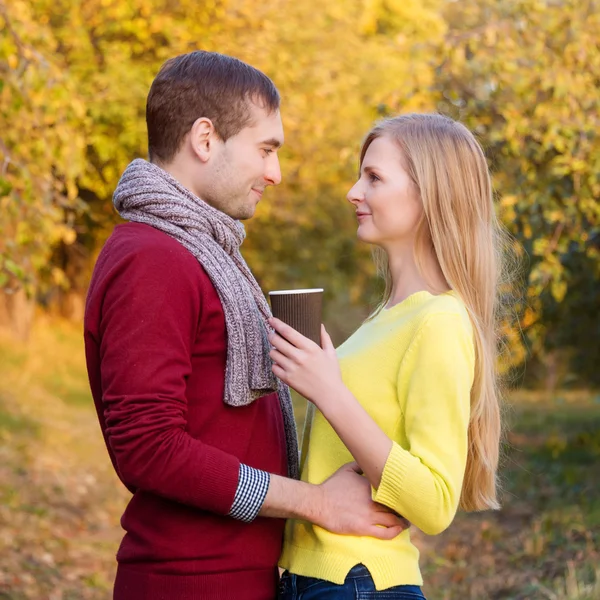 Liefde, relatie, seizoen, vriendschap en mensen concept - gelukkig man en vrouw genieten van gouden herfst vallen seizoen met papier koffie kopjes in het park. Jong koppel hete cofee of thee drinken. — Stockfoto