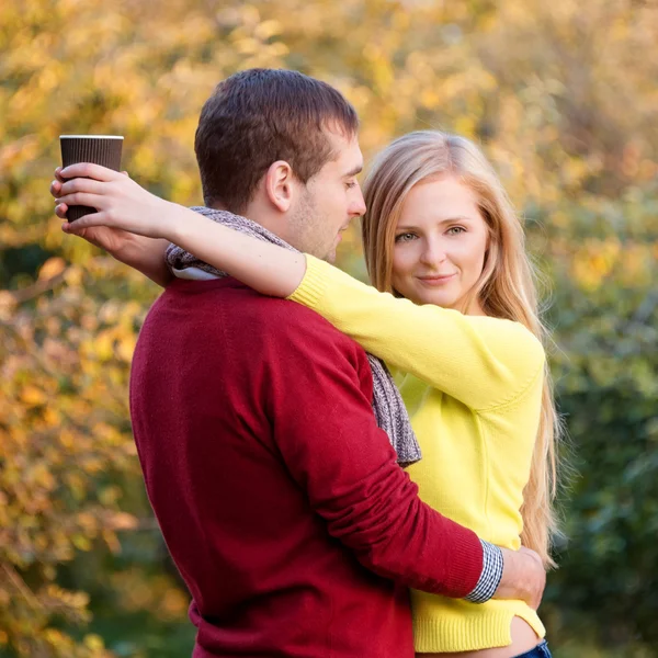 Love, relationship, season, friendship and people concept - happy man and woman enjoying golden autumn fall season with paper coffee cups in the park. Young couple drinking hot cofee or tea. — Stock Photo, Image