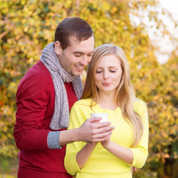 Liefde, relatie, seizoen, vriendschap en mensen concept - gelukkig man en vrouw genieten van gouden herfst vallen seizoen met papier koffie kopjes in het park. Jong koppel hete cofee of thee drinken. — Stockfoto