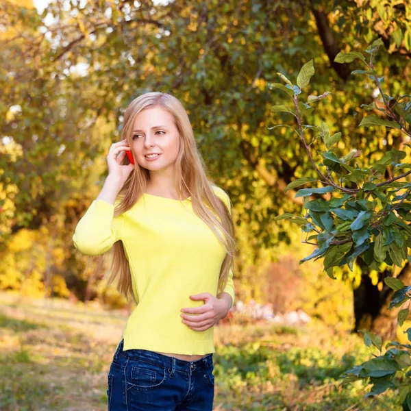 Young blonde woman using a mobile phone walking in autumn park. — Stock Photo, Image