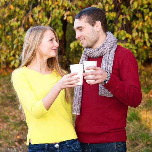 Amor, relacionamento, temporada, amizade e conceito de pessoas - homem feliz e mulher desfrutando de temporada de outono dourado com copos de café de papel no parque. Casal jovem bebendo quente cofee ou chá . — Fotografia de Stock