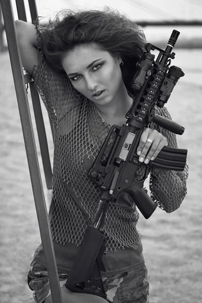 Οπλισμένοι όμορφη νεαρή γυναίκα στο καμουφλάζ με τουφέκι στην παραλία. — Φωτογραφία Αρχείου