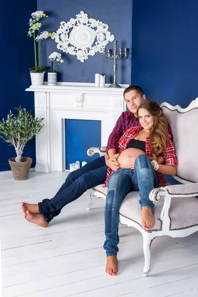 Beautiful pregnant couple relaxing on sofa at home together. Happy family, man and woman expecting a child. — Stock Photo, Image