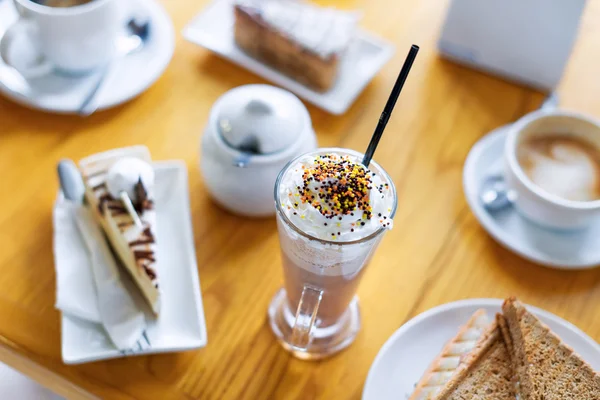 Pequeno-almoço ou lanche à tarde com cappuccino cremoso, sanduíche e bolo na mesa de madeira . — Fotografia de Stock