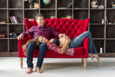 Güzel hamile çift birlikte evde kanepede rahatlatıcı. Mutlu aile, erkek ve kadın bir çocuk bekliyor.