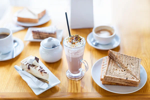 Desayuno o merienda con capuchino cremoso, sándwich y pastel en mesa de madera . —  Fotos de Stock