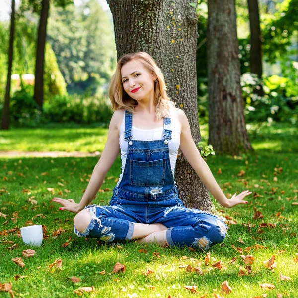 Happy blonde woman enjoying nature sitting on green grass with cup of coffee. Freedom concept — Stock Photo, Image