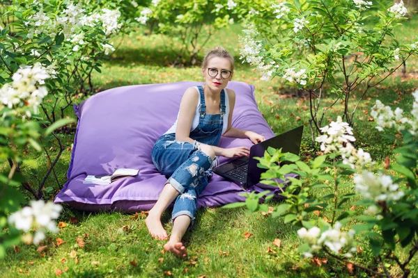 Frilansare som jobbar i trädgården. Skriva, surfa på internet. Ung kvinna koppla av och ha kul i parken område. Distansutbildning, frilansbegrepp. — Stockfoto