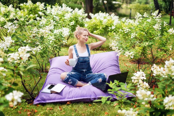 Frilansare som arbetar i trädgården. Skriva, surfa på Internet. Ung kvinna avkopplande och ha kul i parkområdet dricka kaffe. Distansutbildning, frilans koncept. — Stockfoto