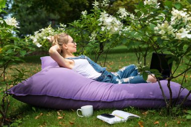 Bahçede çalışan serbest çalışan biri. Yazmak, internette sörf yapmak. Genç bir kadın park alanında rahatlıyor ve eğleniyor. Uzaklık eğitimi, serbest çalışma kavramı.