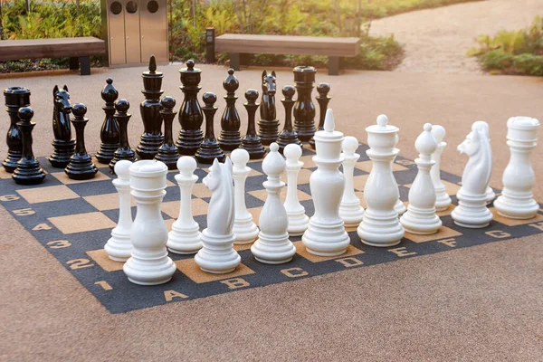 Outdoor chess board with big plastic pieces. Giant size chess in public area zone. Close up big pieces and giant chess board of street chess in the park.