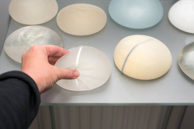 Göğüs büyütmek için kadın eli silikon implantlara dokunuyor. Estetik estetik ameliyat. Esnekliğin, yumuşaklığın, çeşitli tiplerdeki güvenilirliğin ve farklı boyutlardaki silikon implantların gösterimi.