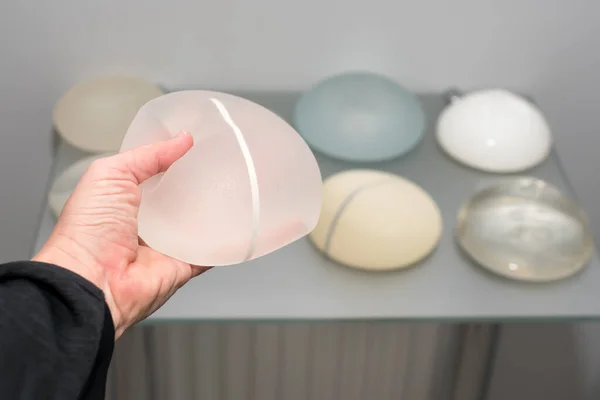 Göğüs büyütmek için kadın eli silikon implantlara dokunuyor. Estetik estetik ameliyat. Esnekliğin, yumuşaklığın, çeşitli tiplerdeki güvenilirliğin ve farklı boyutlardaki silikon implantların gösterimi.
