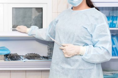 Doktorun eli ameliyathanede damar kıskaçlarını tutuyor. Steril kutuda ameliyat aletleri. Tıbbi ve cerrahi konsepti