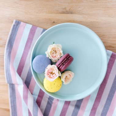 Ahşap zemin üzerinde güller olan renkli badem kurabiyeleri. Fransız pastası. Çiçekli şekerler.