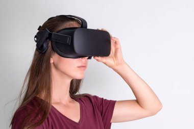 Sanal gerçeklik gözlüğü takan genç bir kadın. Bağlantı, teknoloji, yeni nesil, ilerleme kavramı. Sanal gerçeklikte nesnelere dokunmaya çalışan bir kız. Stüdyo çekimi gri üzerine.