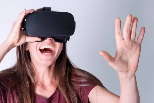 Young woman wearing virtual reality goggles headset, vr box. Connection, technology, new generation, progress concept. Girl trying to touch objects in virtual reality. Studio shot on gray.