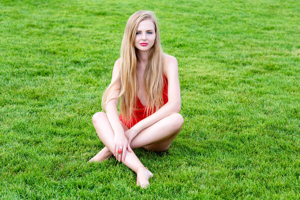 Young woman in red swimsuit sunbathing on the grass. Summer leisure, outdoors in the park at luxury resort