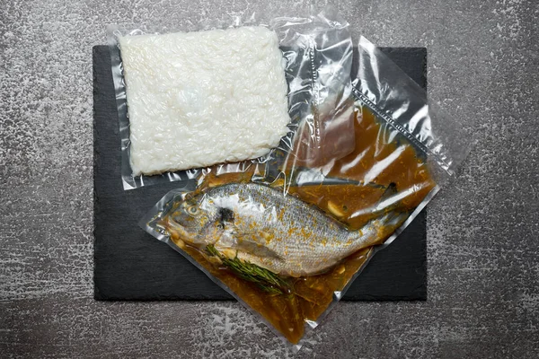 Products in vacuum packaging on black slate board. Fish and rice, vacuum sealed food ready for sous vide cooking. Sous-vide, new technology cuisine, new normal in quarantine pandemic time.