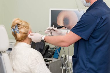 Otolaryngologist otitus muayenesi yapıyor, video otoskopisi prosedürü. Duyma kliniği. Maske takan ve eldiven takan ENT doktoru hastanın kulağını muayene ediyor..