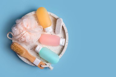 Mavi arka planda kaplıca ve banyo aksesuarları için kozmetik ürünler. Şampuan, saç kremi ve mermer tepside bez bulunan duş jeli için renkli plastik kaplar. Güzellik, seyahat konsepti, düz yatak