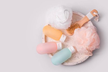 Gri arka planda kaplıca ve banyo aksesuarları için kozmetik ürünler. Şampuan, saç kremi ve mermer tepside bez bulunan duş jeli için renkli plastik kaplar. Güzellik, seyahat konsepti, düz yatak
