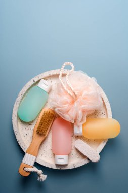 Mavi arka planda kaplıca ve banyo aksesuarları için kozmetik ürünler. Şampuan, saç kremi ve mermer tepside bez bulunan duş jeli için renkli plastik kaplar. Güzellik, seyahat konsepti, düz yatak